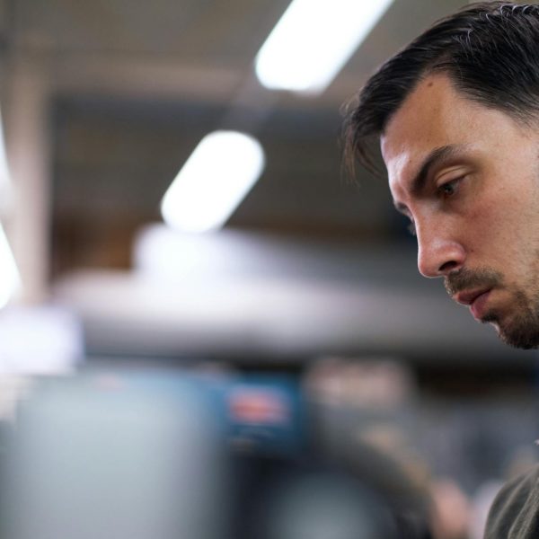 A man in a workshop focuses intently, surrounded by blurred tools and equipment.