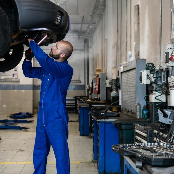 Mechanic inspecting a raised car in an auto workshop for maintenance and repair services.